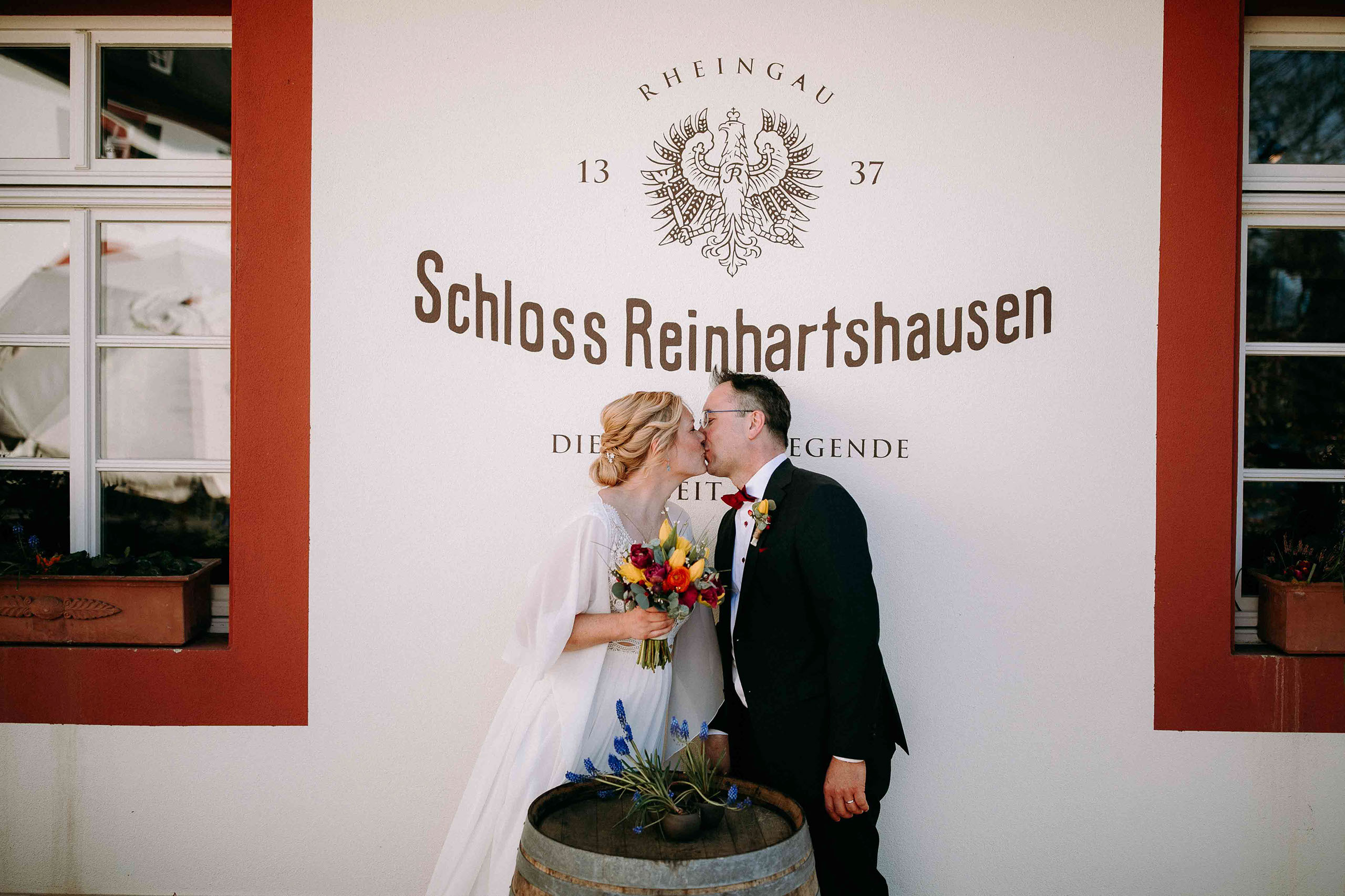 Brautpaar küsst sich vor dem Logo von Schloss Reinhartshausen – Hochzeitslocation Rheingau