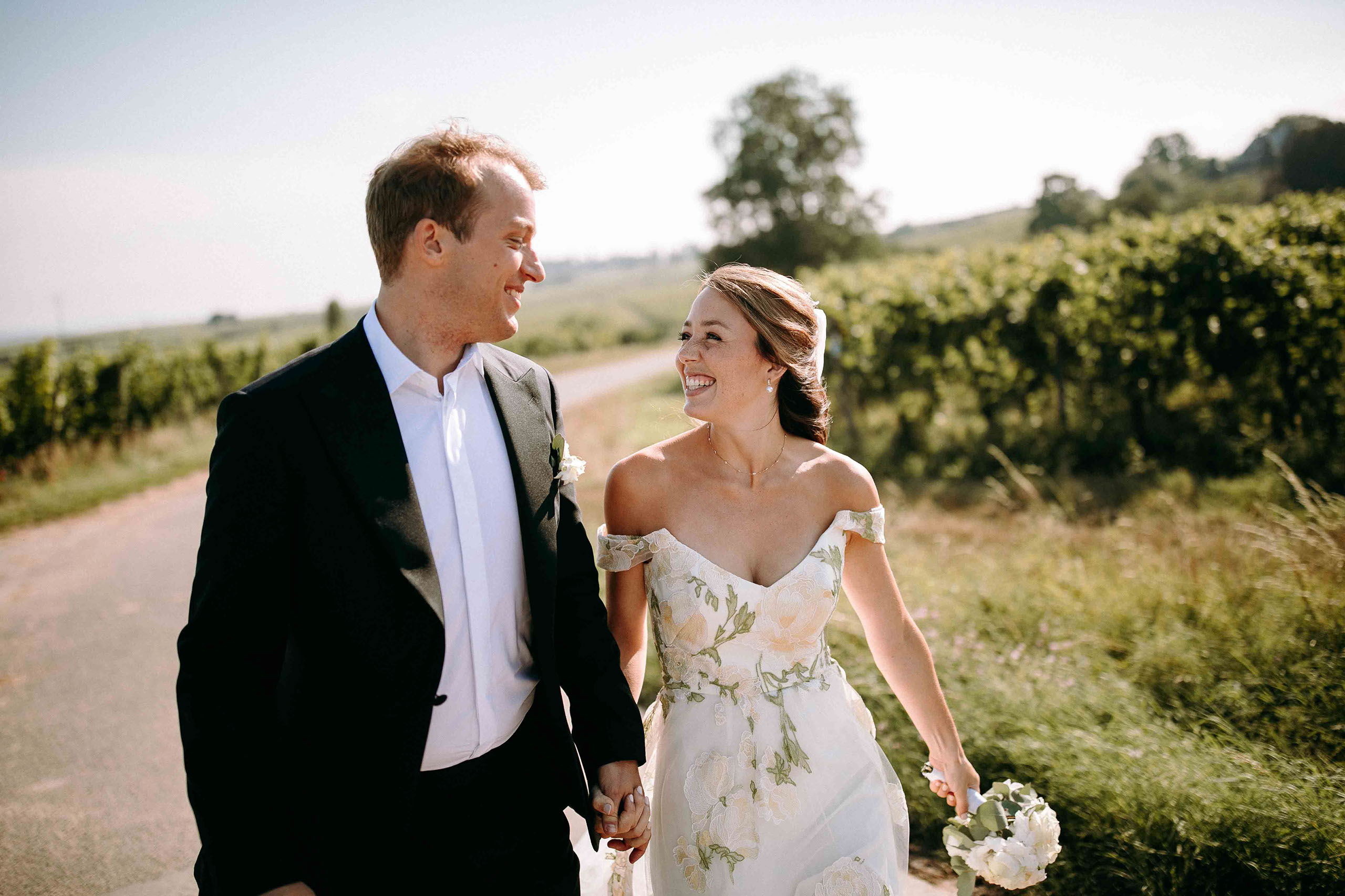 Fröhliches Brautpaar spaziert durch die Weinberge des Schloss Vollrads – festgehalten vom Hochzeitsfotograf im Rheingau.