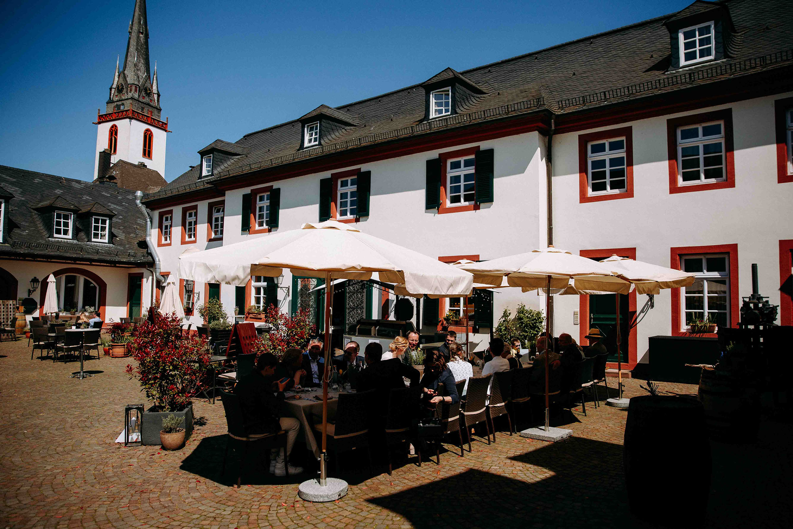 Gäste genießen die Hochzeitsfeier unter Sonnenschirmen im Innenhof von Schloss Reinhartshausen – Hochzeitsfotograf Rheingau