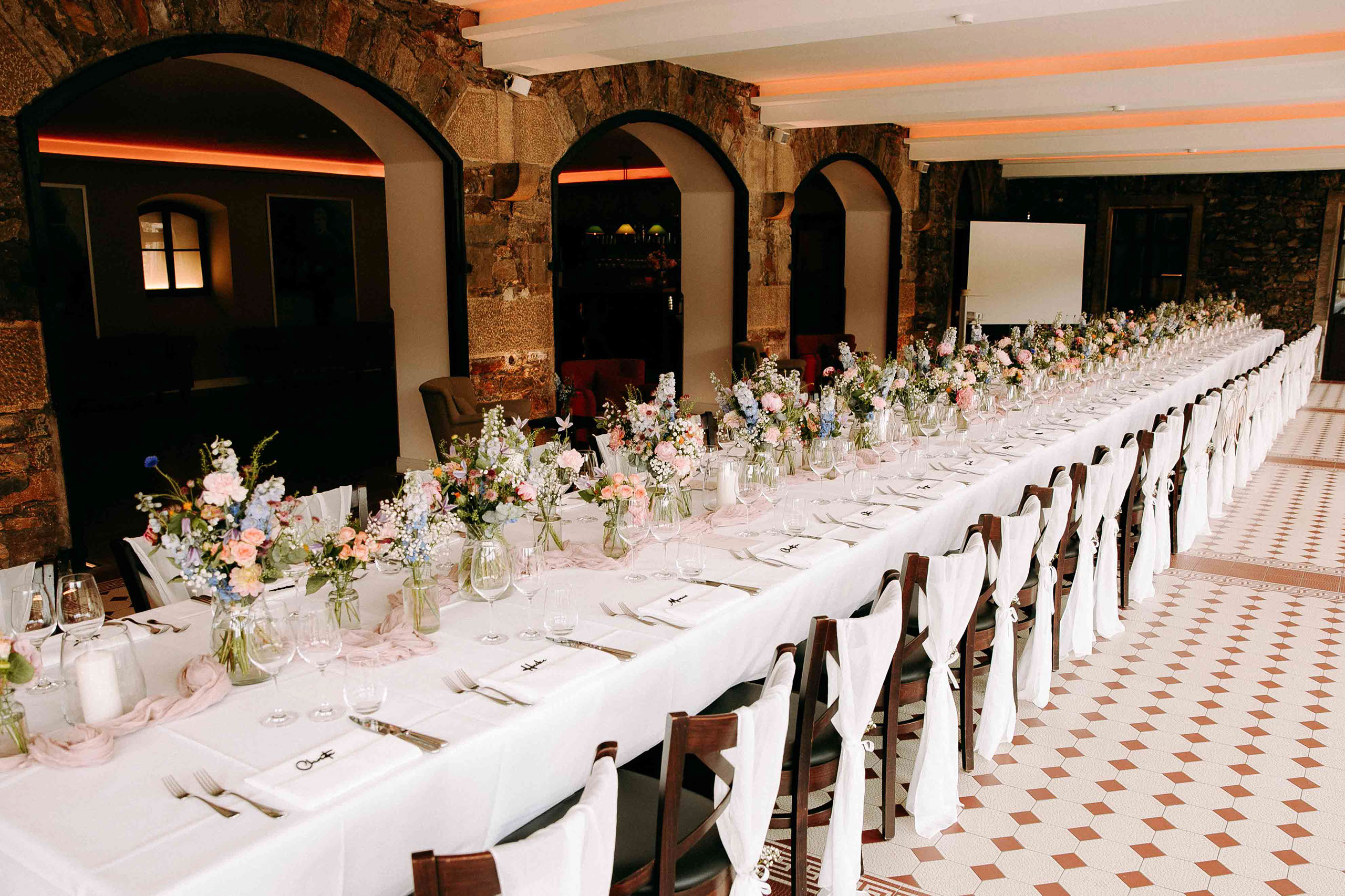 Langer Hochzeitstisch mit eleganter Blumendekoration im Festsaal der Burg Reichenstein – perfekte Hochzeitslocation im Rheingau.