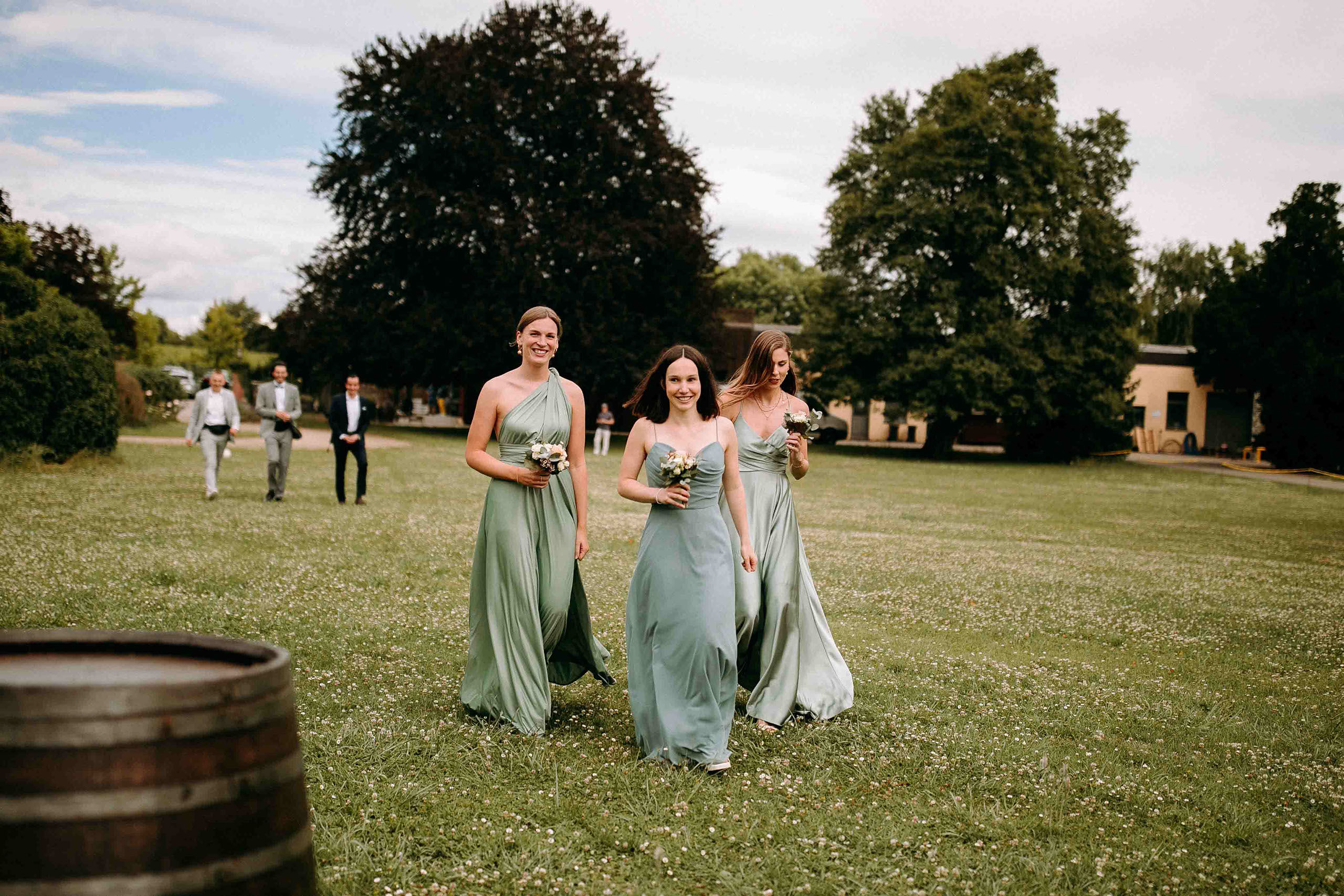 Drei Brautjungfern in grünen Kleidern laufen lachend über die Wiese beim Draiser Hof