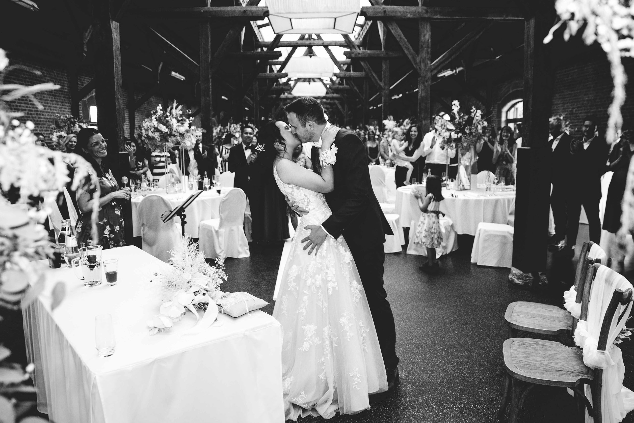 Romantischer Hochzeitskuss im Güterbahnhof Bad Homburg – Schwarz-Weiß-Aufnahme mit Gästen