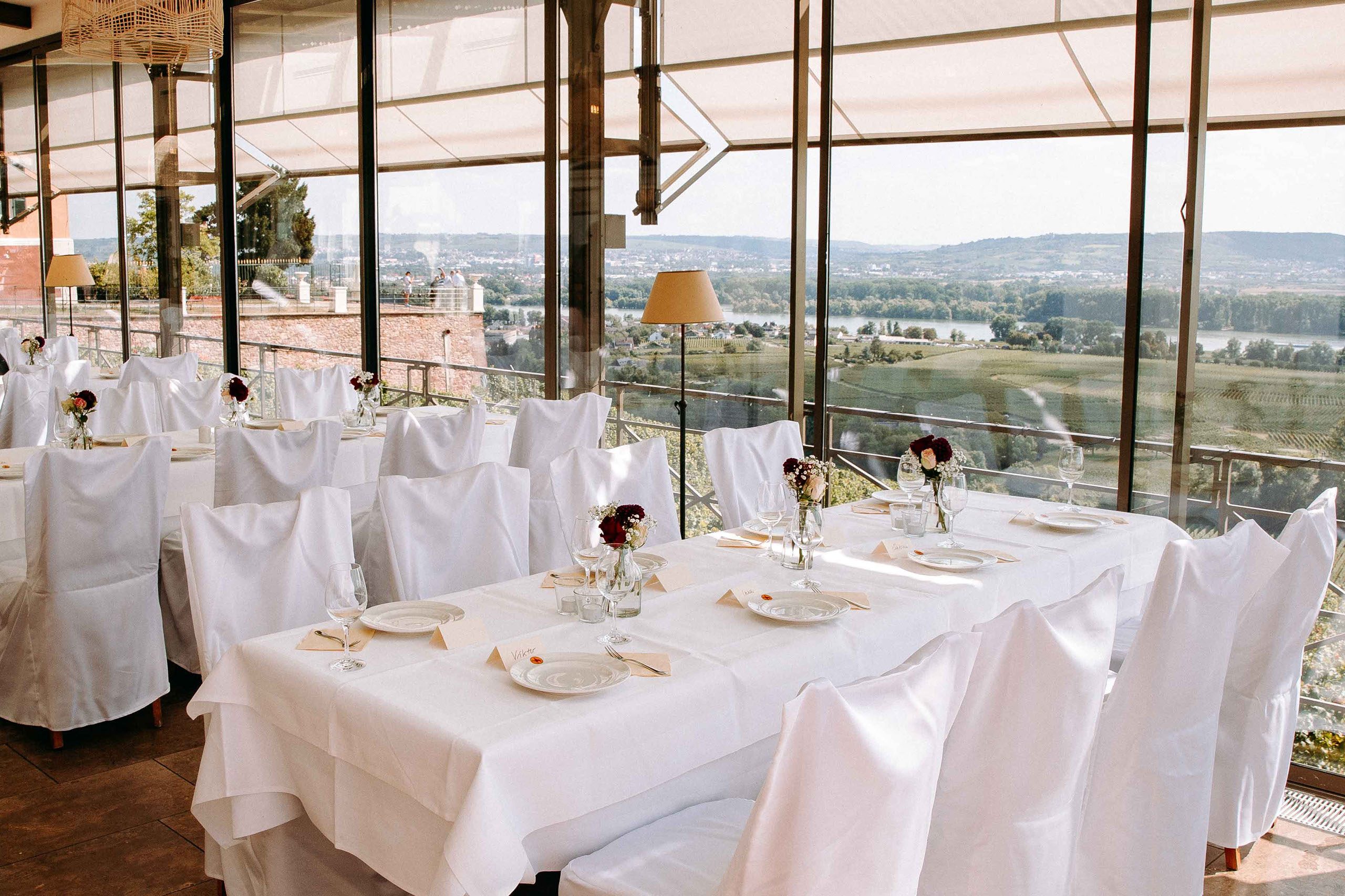 Romantisch gedeckte Hochzeitstische mit Ausblick auf das Rheintal im verglasten Wintergarten von Schloss Johannisberg