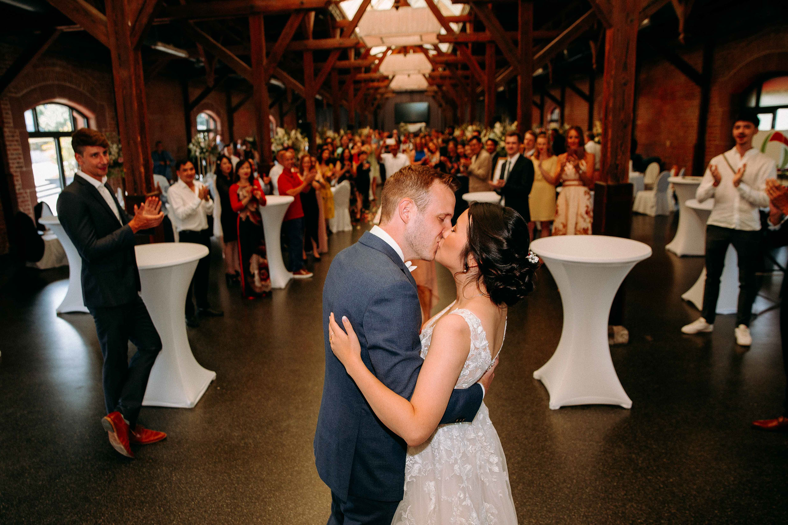 Hochzeitskuss in industriellem Ambiente im Güterbahnhof Bad Homburg – Brautpaar umgeben von Hochzeitsgästen