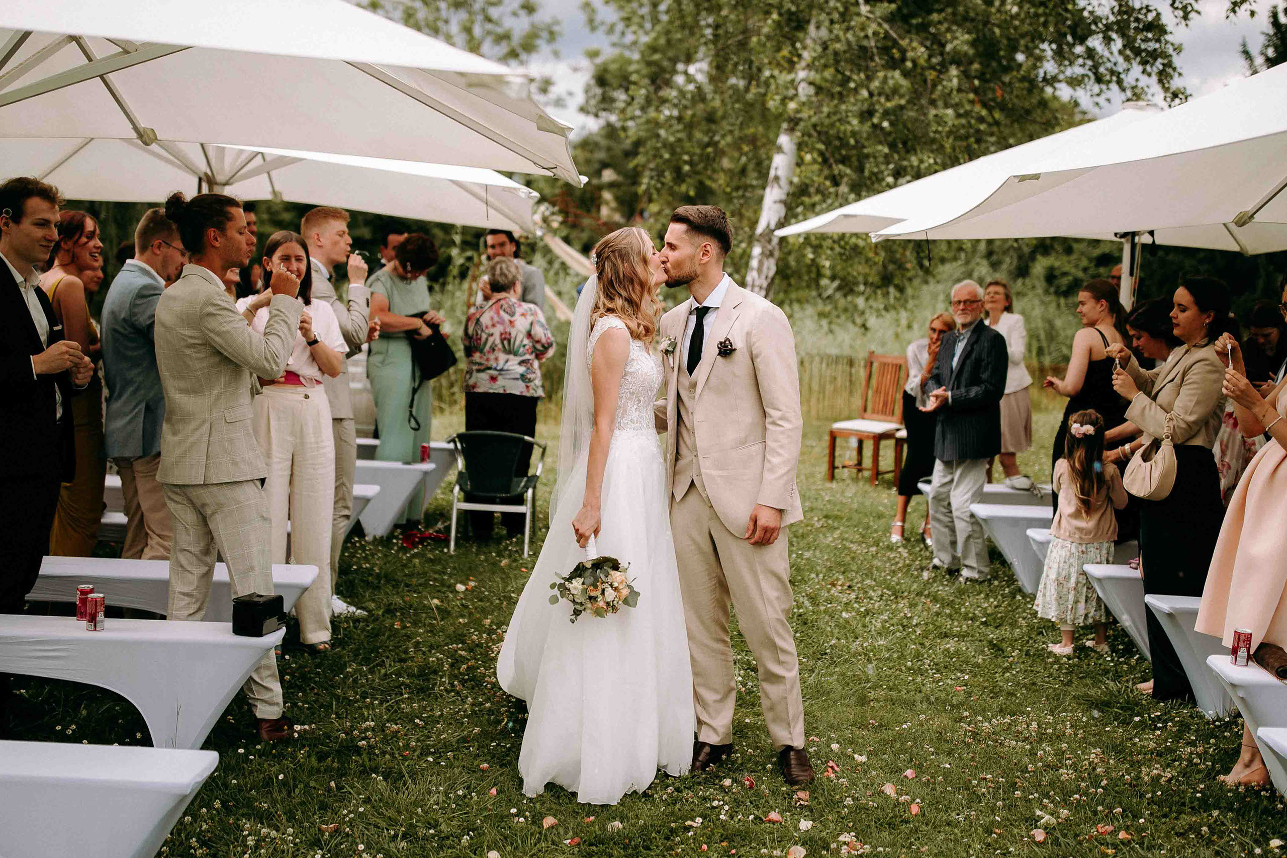 Brautpaar küsst sich nach der Zeremonie inmitten applaudierender Gäste