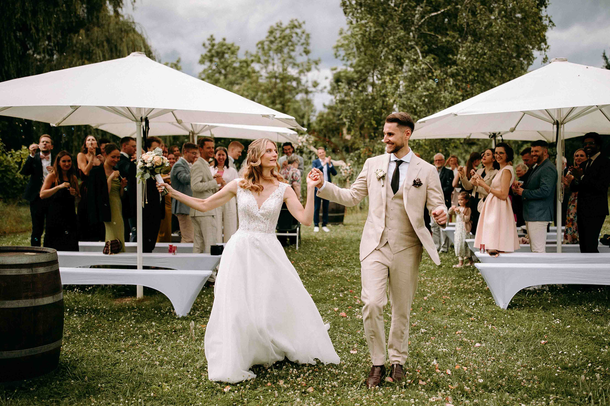 Frisch verheiratetes Brautpaar zieht Hand in Hand lächelnd durch die Reihen