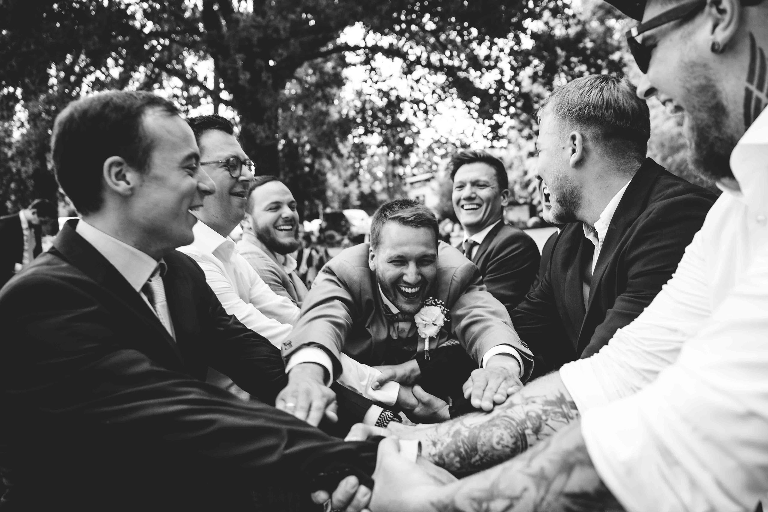 Lachender Bräutigam umringt von seinen Freunden – emotionale Hochzeitsfotos Burg Schwarzenstein Rheingau.