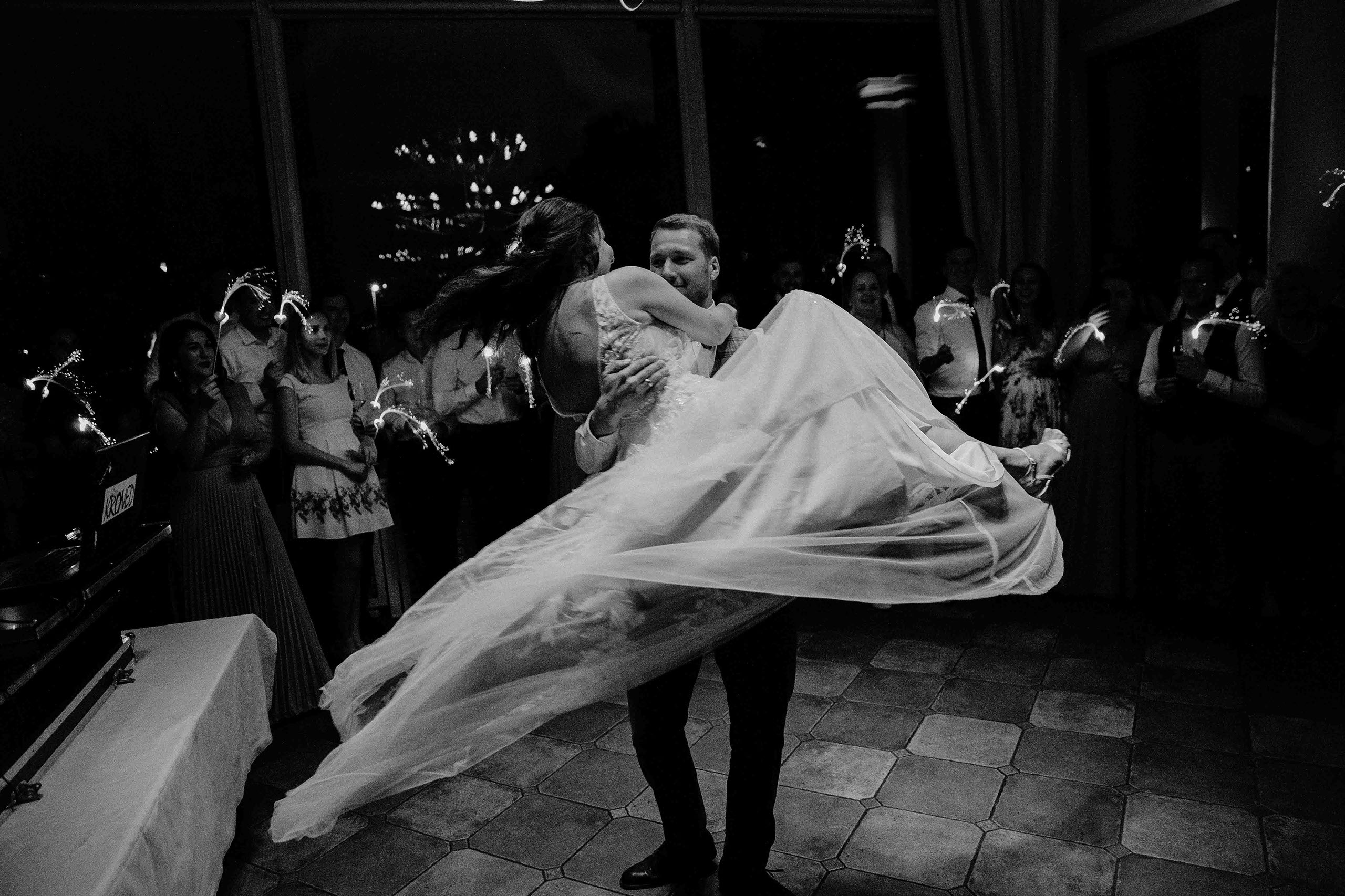 Der Bräutigam hebt die Braut beim Hochzeitstanz umringt von Gästen mit Wunderkerzen in der Hochzeitslocation Burg Schwarzenstein – Hochzeitsfoto