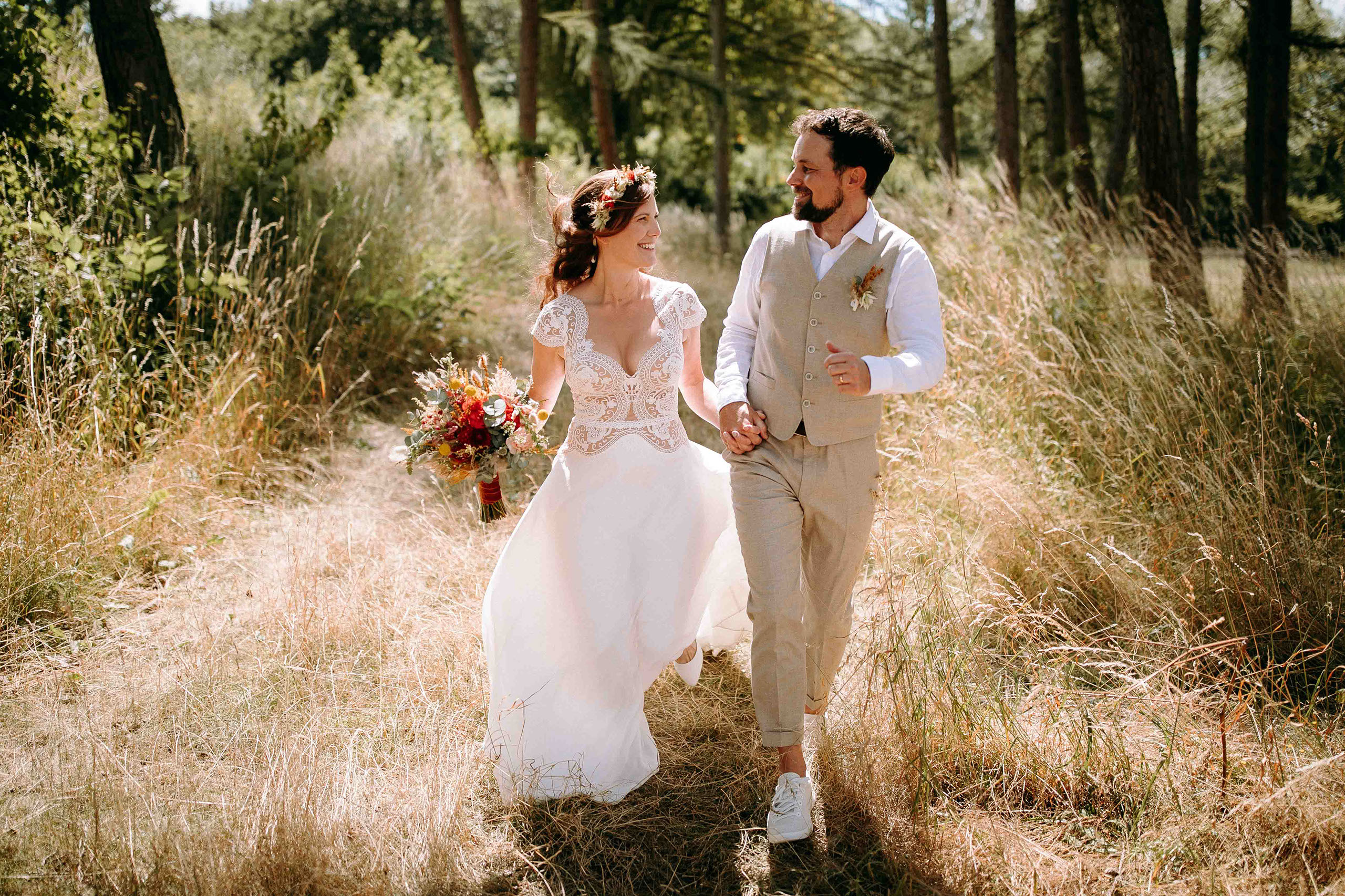 Das Brautpaar läuft glücklich Hand in Hand durch einen sonnigen Waldweg im Hessenpark.