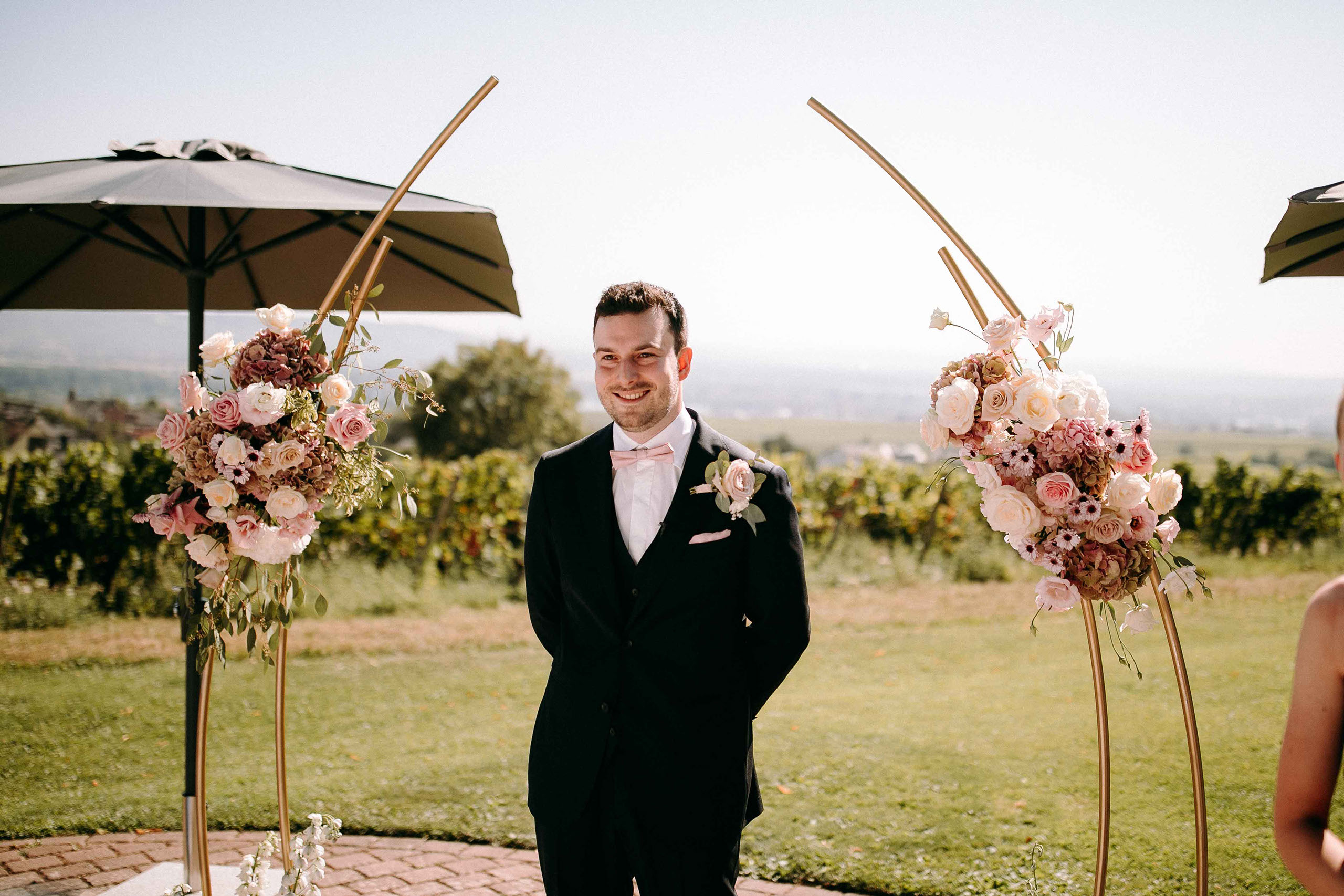 Der Bräutigam wartet gespannt unter einem mit Blumen geschmückten Bogen bei der Trauung in der Hochzeitslocation Burg Schwarzenstein