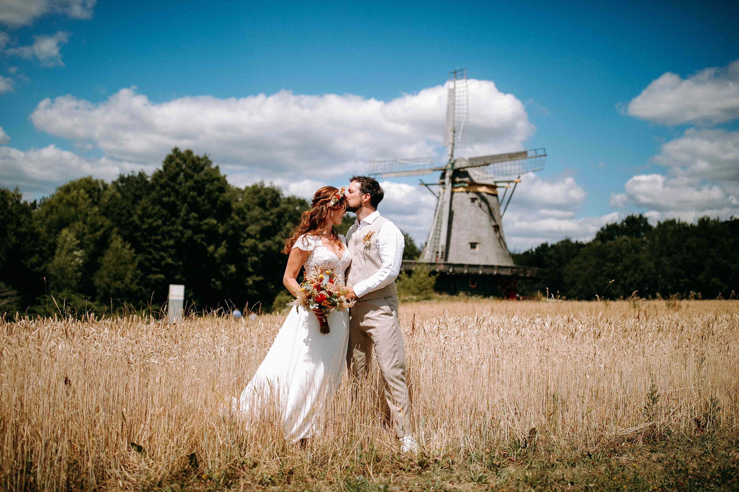 Brautpaar steht in einem Feld mit einer historischen Windmühle im Hintergrund.