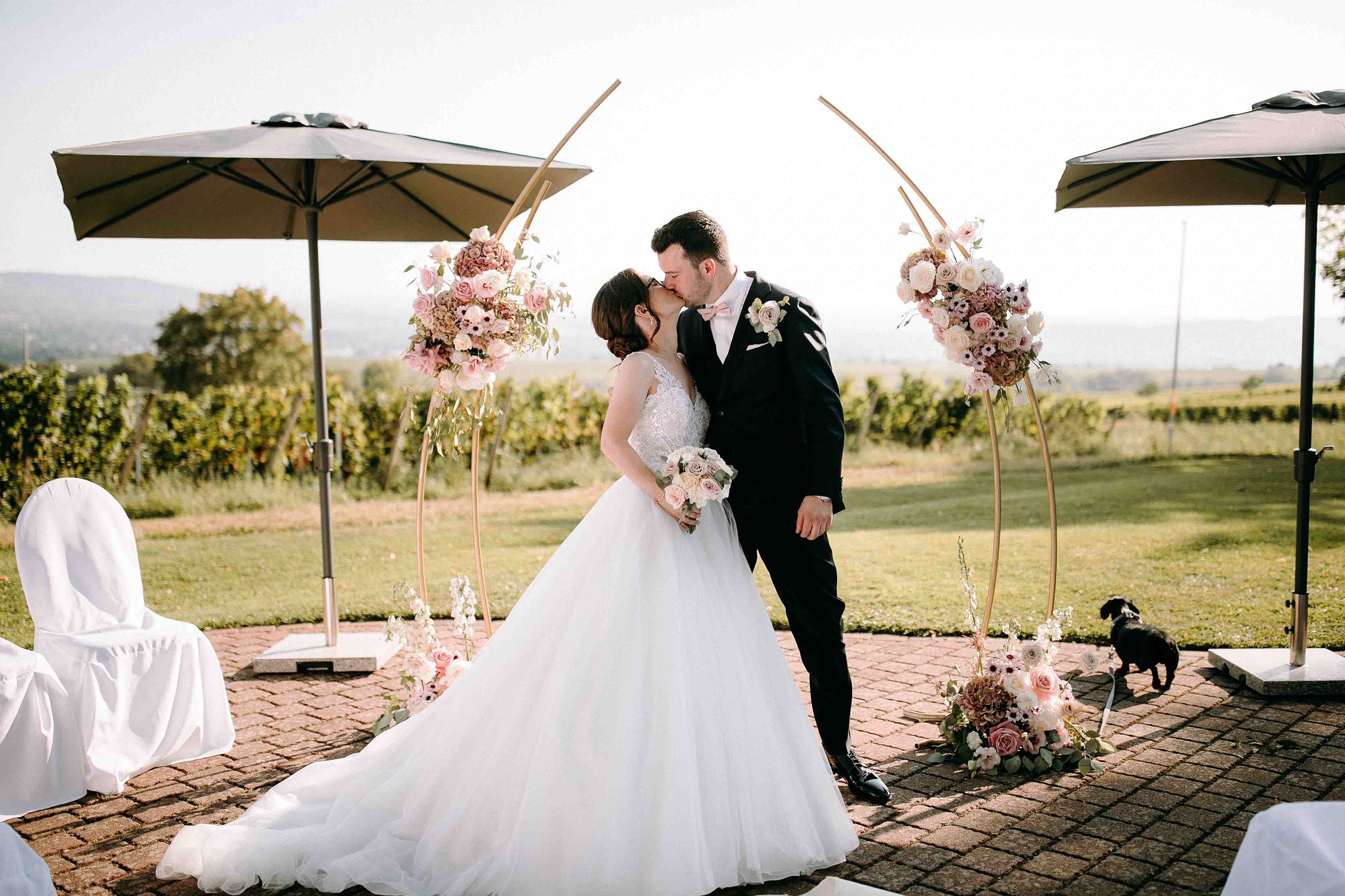 Das Brautpaar küsst sich unter dem goldenen Traubogen bei der Hochzeitslocation Burg Schwarzenstein – Hochzeitsfotograf Rheingau.