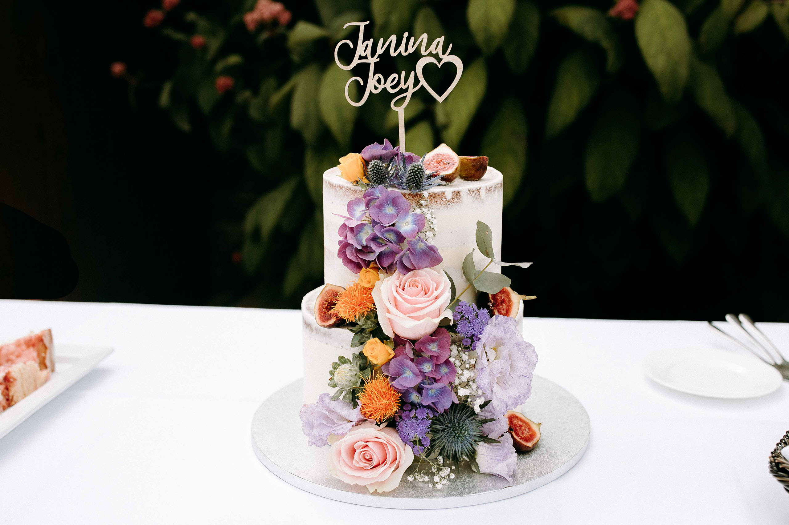 Zweistöckige Hochzeitstorte mit Blumenarrangement auf weißem Tisch – Hochzeitslocation Burg Reichenstein