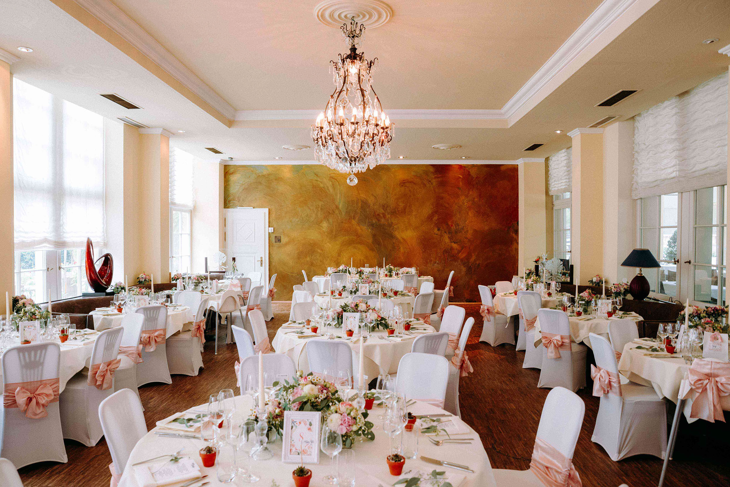 Runder Hochzeitstisch mit Blumen und Kerzen im stilvollen Festsaal der Orangerie Bad Homburg.