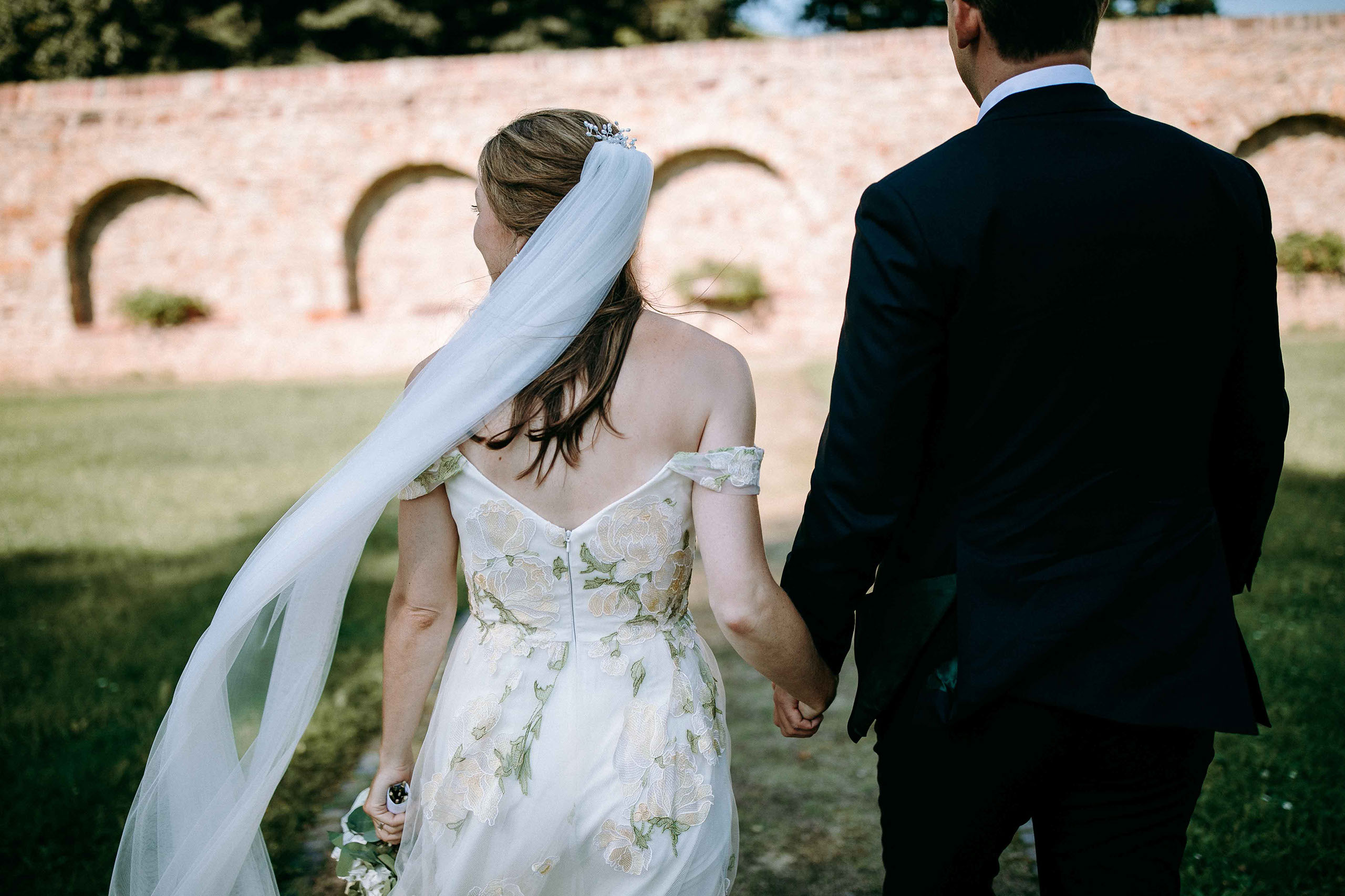 Brautpaar Hand in Hand im grünen Garten mit Steinmauer