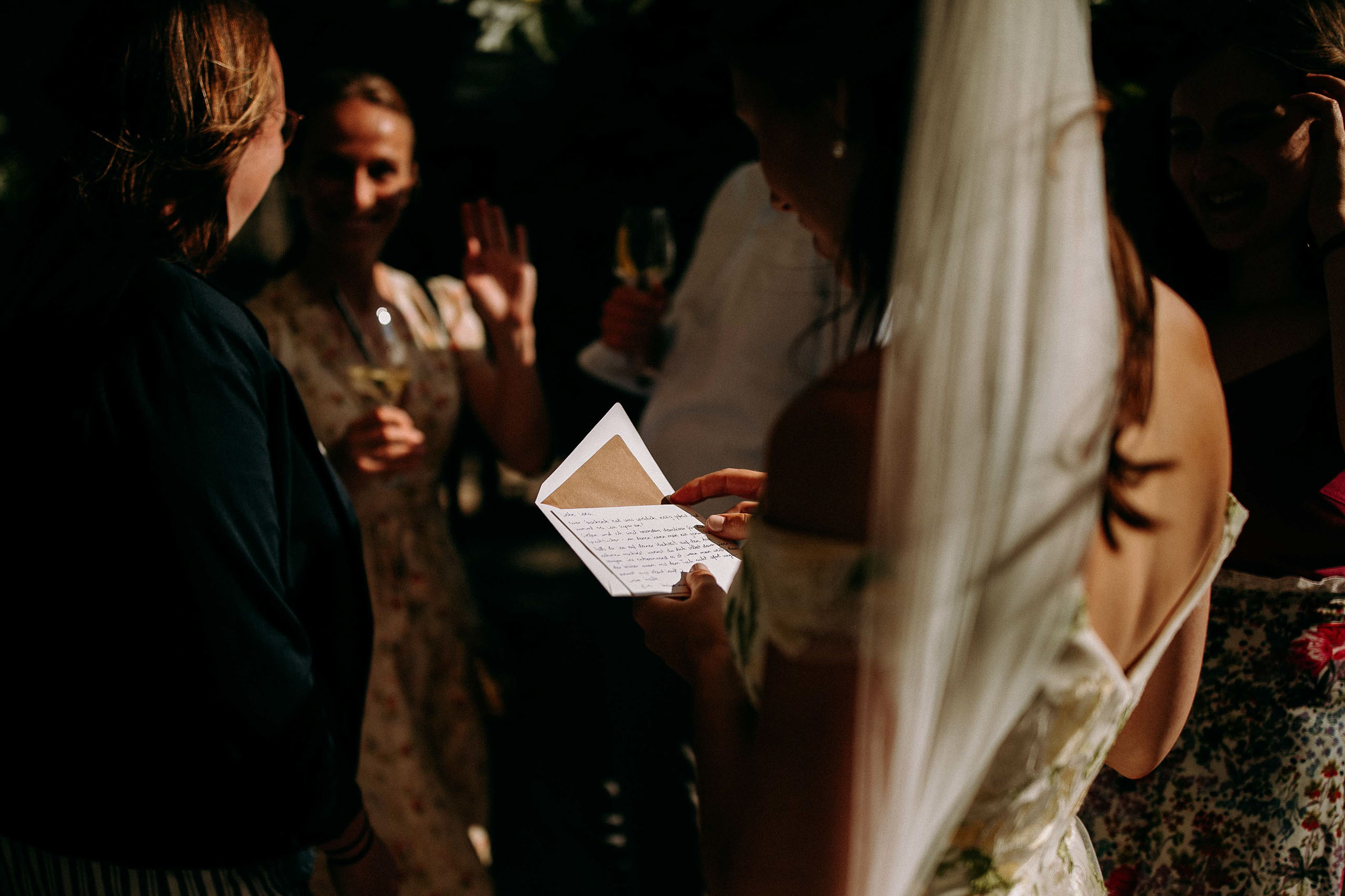 Braut im Kleid liest Karte umgeben von Gästen