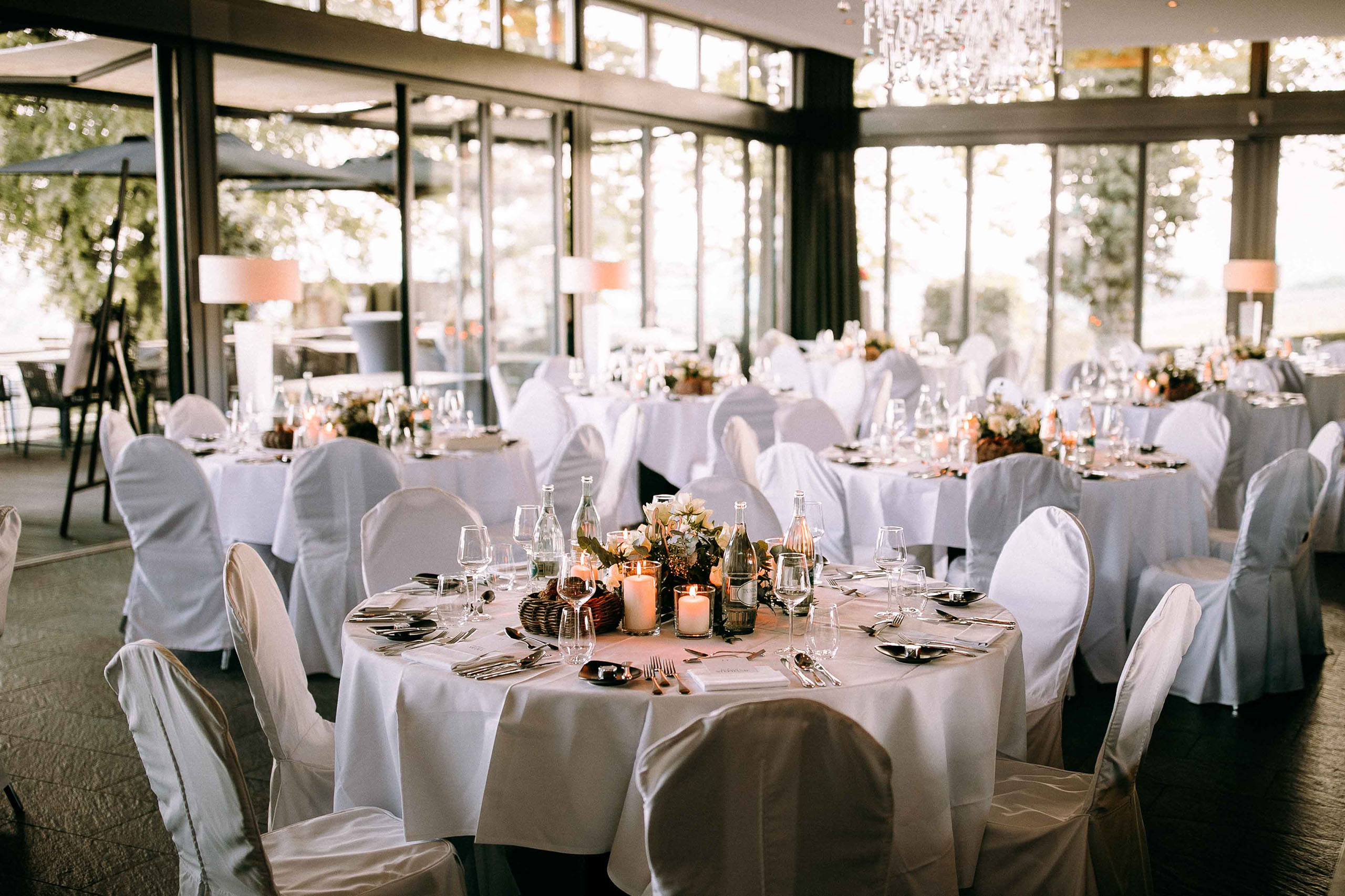 Runde Hochzeitstische mit weißen Hussen, Blumenarrangement und Kerzen auf Burg Schwarzenstein.