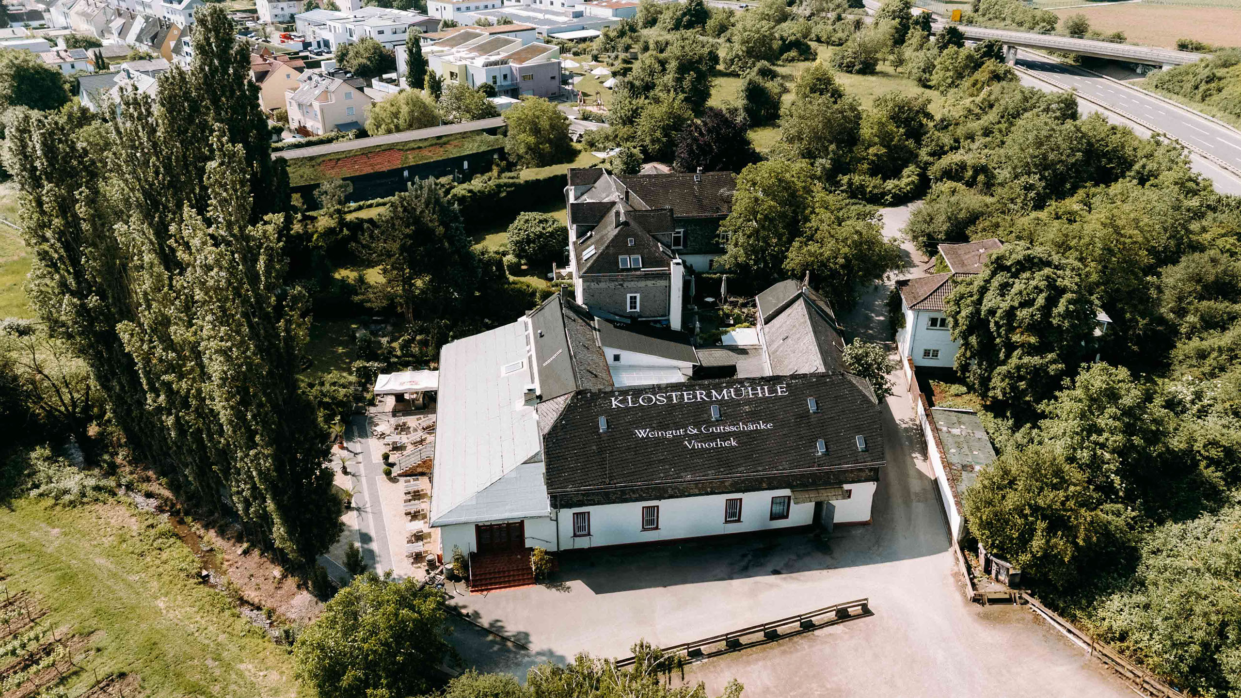 Luftbild der Klostermuehle mit beschriftetem Dach, Innenhofbestuhlung und angrenzendem Weinberg – authentische Hochzeitslocation im Rheingau.